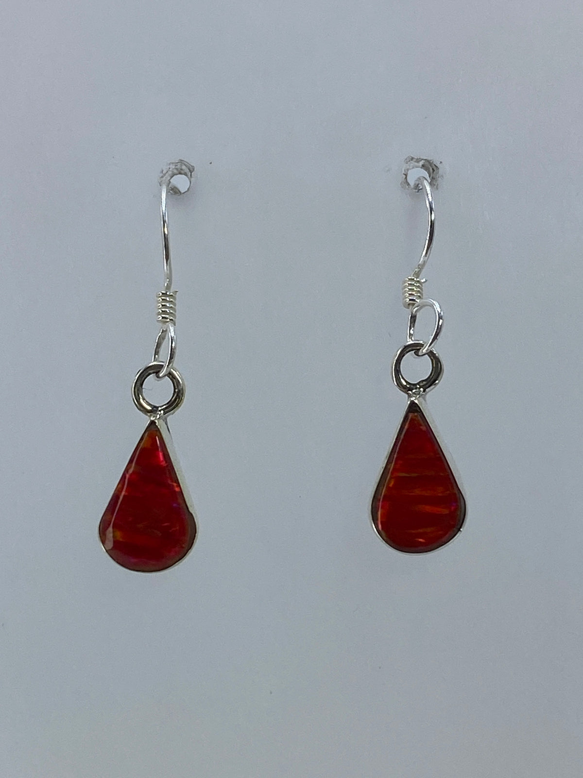 Aretes de plata con ópalo de fuego rojo, colgando frente a fondo blanco