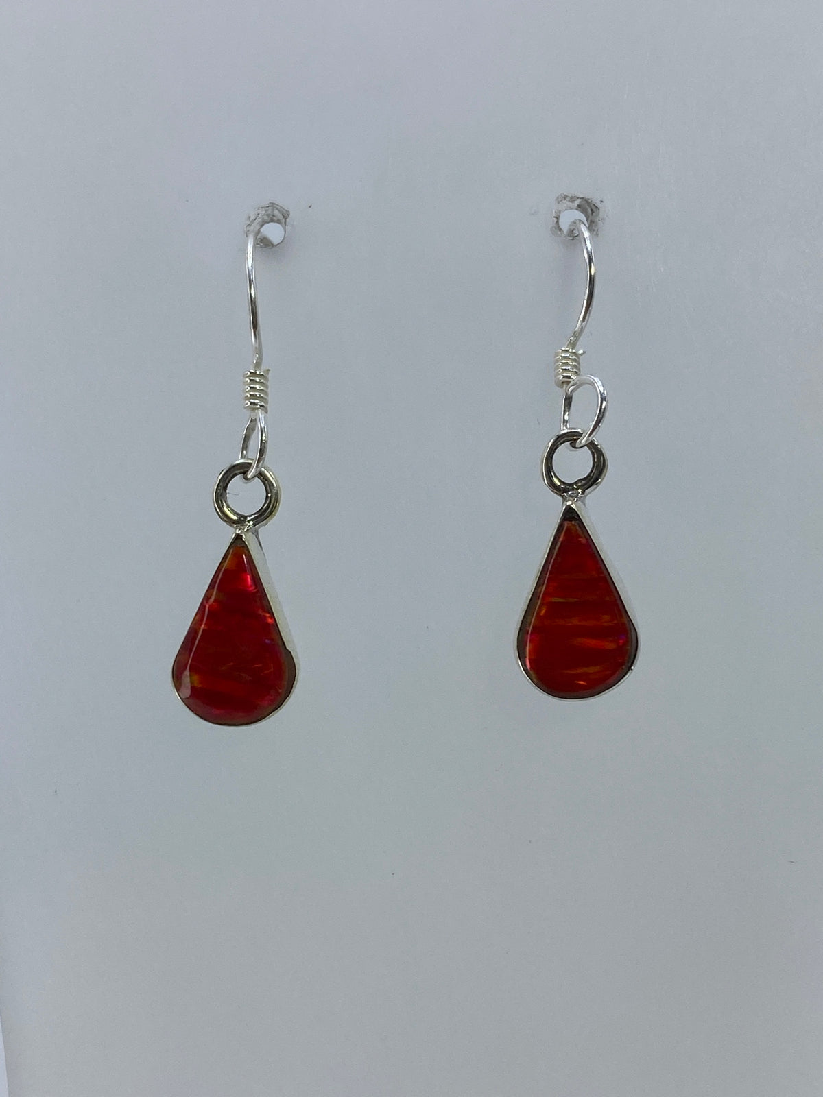 Detalle de los aretes mostrando el ópalo de fuego rojo engastado y el gancho de plata