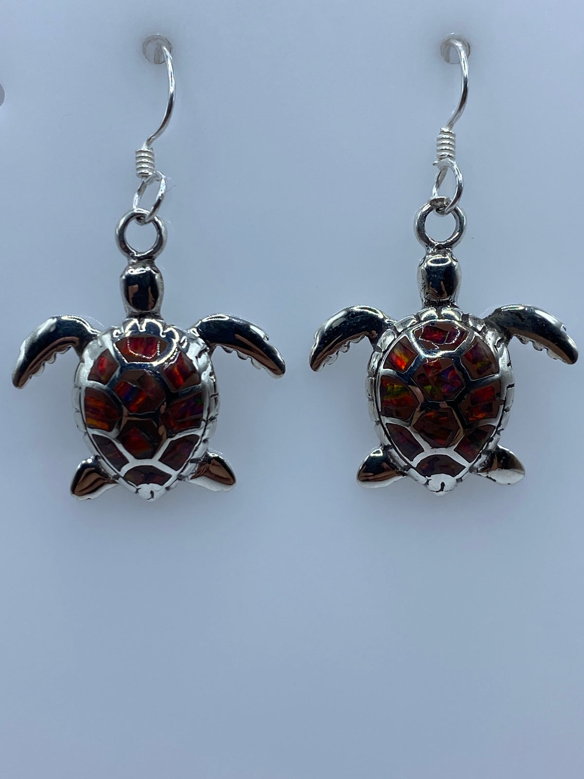 Par de aretes de plata con ópalo de fuego multicolor, colgando sobre fondo blanco