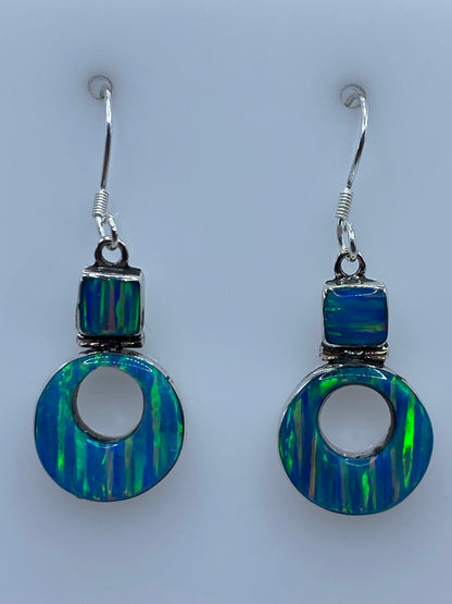Aretes de plata 950 con opalo de fuego azul cielo, engaste a mano, colgando sobre fondo claro