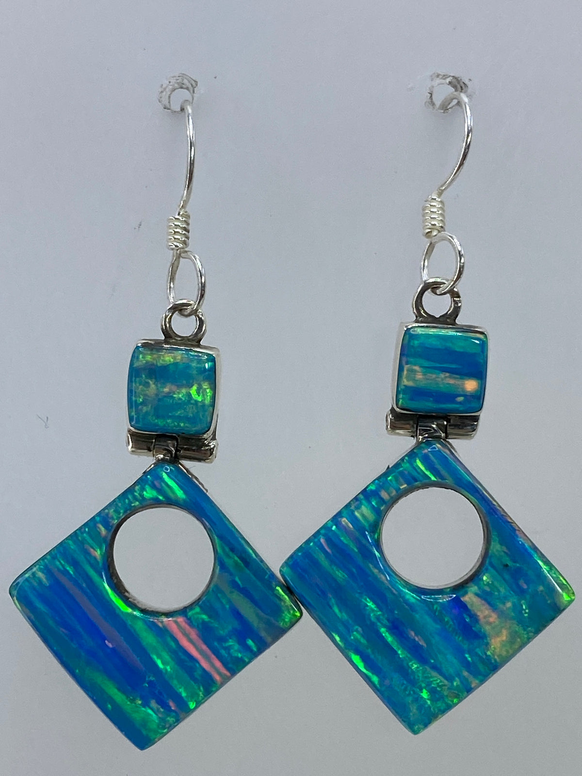 Aretes de ópalo colocados sobre una tela azul brillante, viéndose el juego de luces en la piedra