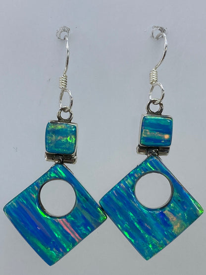 Aretes de ópalo colocados sobre una tela azul brillante, viéndose el juego de luces en la piedra