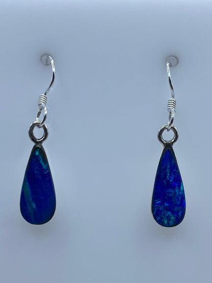 Par de aretes de plata con ópalo de fuego azul colgando sobre fondo gris