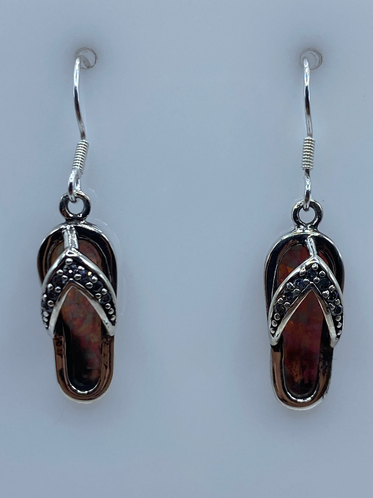 Par de aretes de plata con ópalo de fuego multicolor engastado a mano, colgando sobre fondo azul