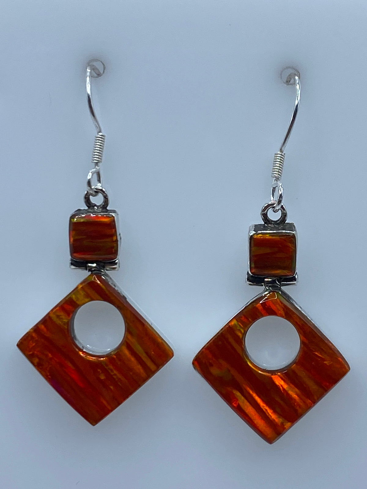 Par de aretes de plata con ópalo de fuego naranja colgando sobre fondo blanco