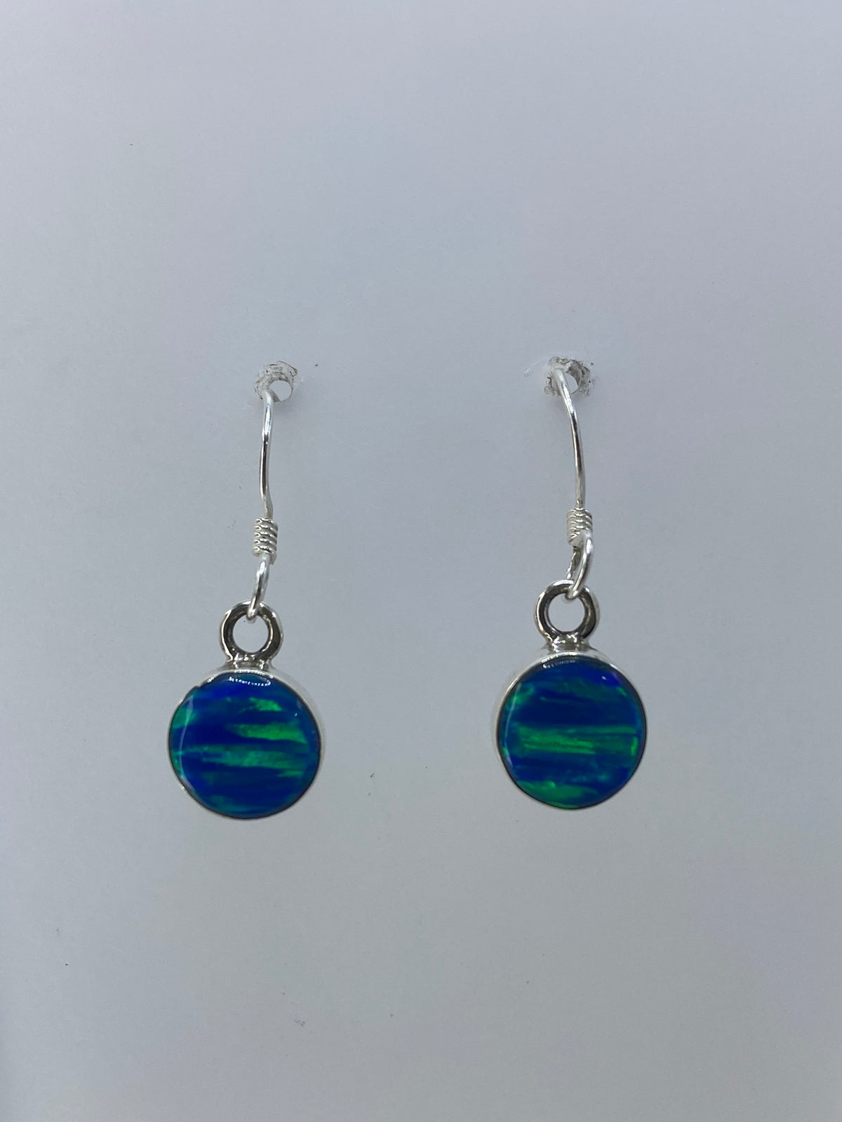 Aretes de ópalo de fuego mostrando juegos de luz verde, azul y naranja en el engaste