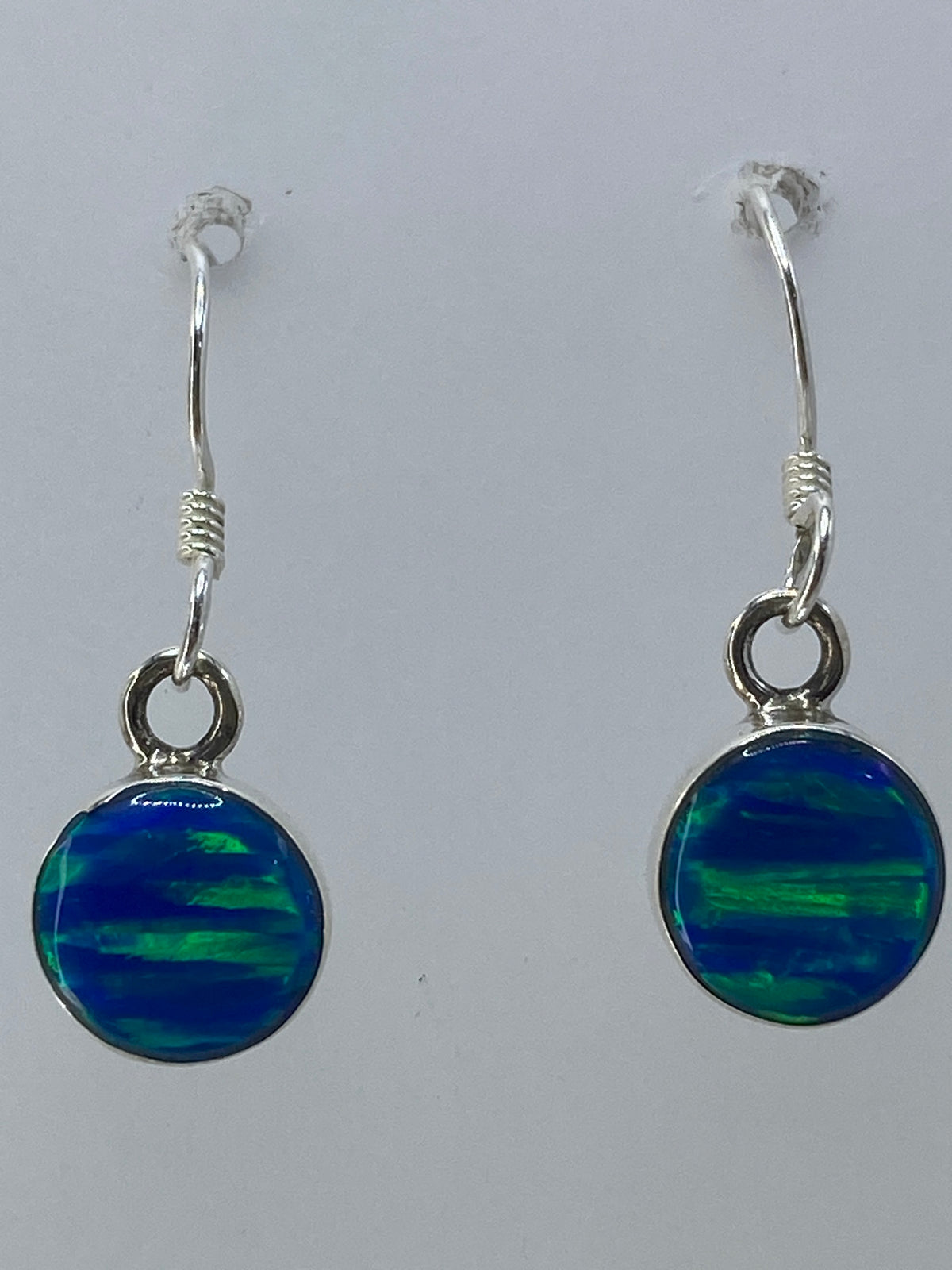 Vista frontal del par de aretes sobre fondo blanco, ópalo multicolor en detalle