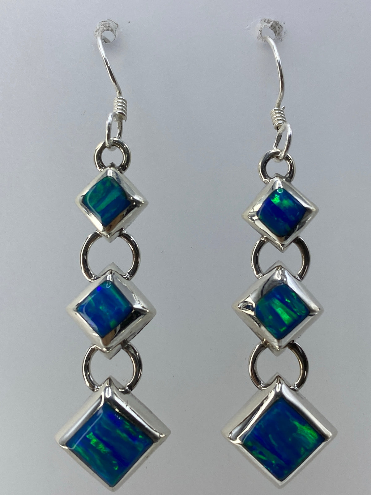 Aretes en la mano mostrando el tamaño real de 4.5 cm y el brillo verde del ópalo