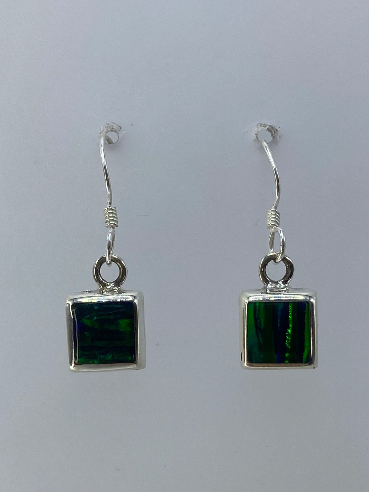 Par de aretes de plata 925 con ópalo de fuego verde limón engastado, colgando sobre fondo blanco
