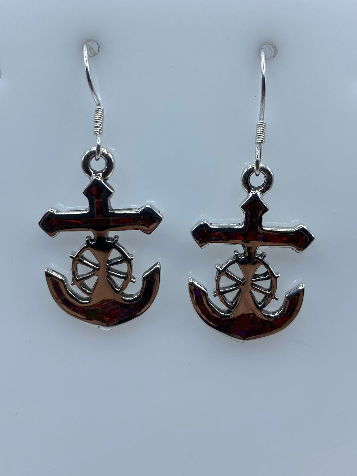 Aretes de plata 950 con ópalo de fuego multicolor en diseño de ancla marinera, sostenidos en una mano