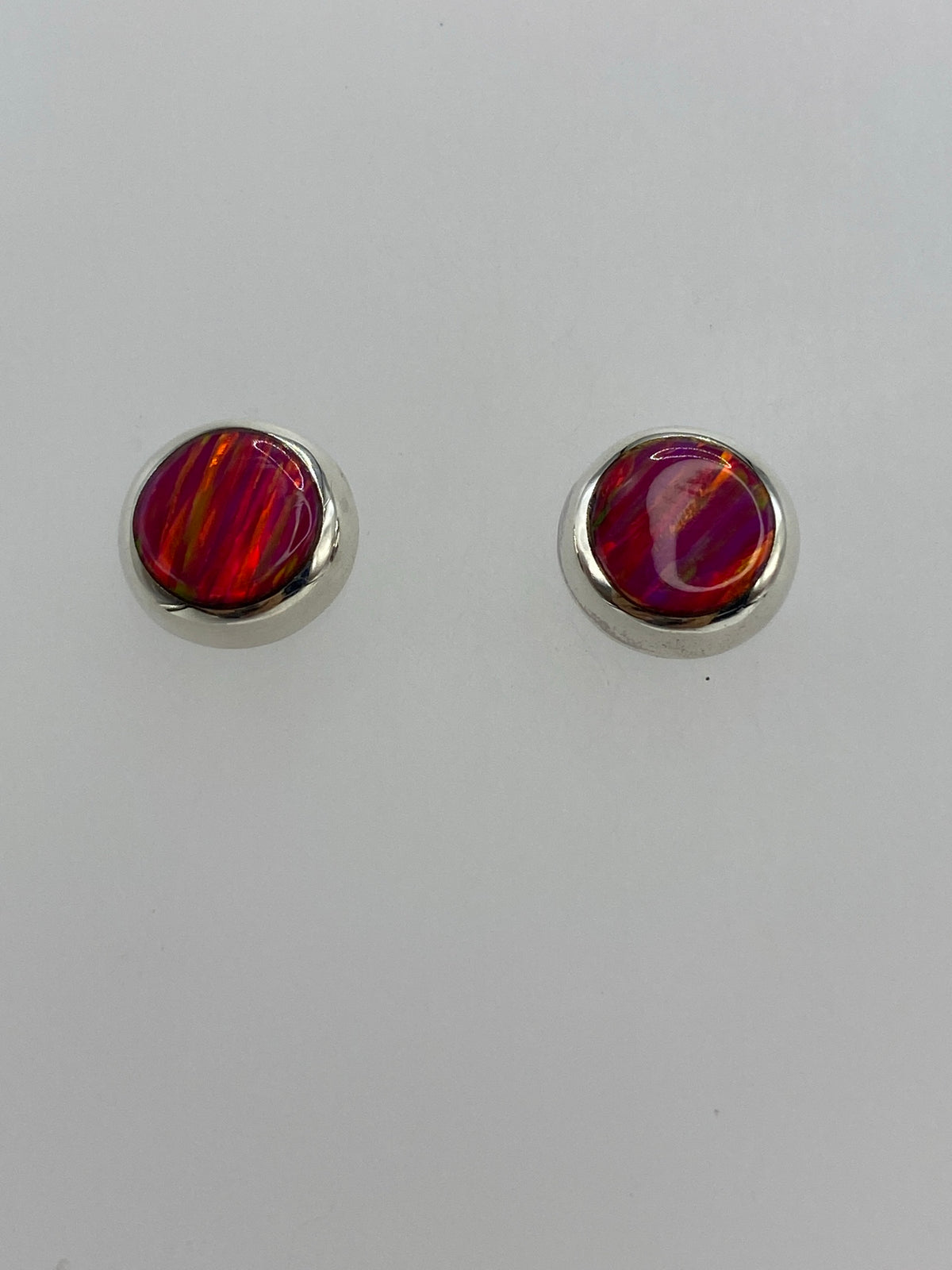 Aretes ópalo de fuego mostrando la iridiscencia rosa bajo luz natural