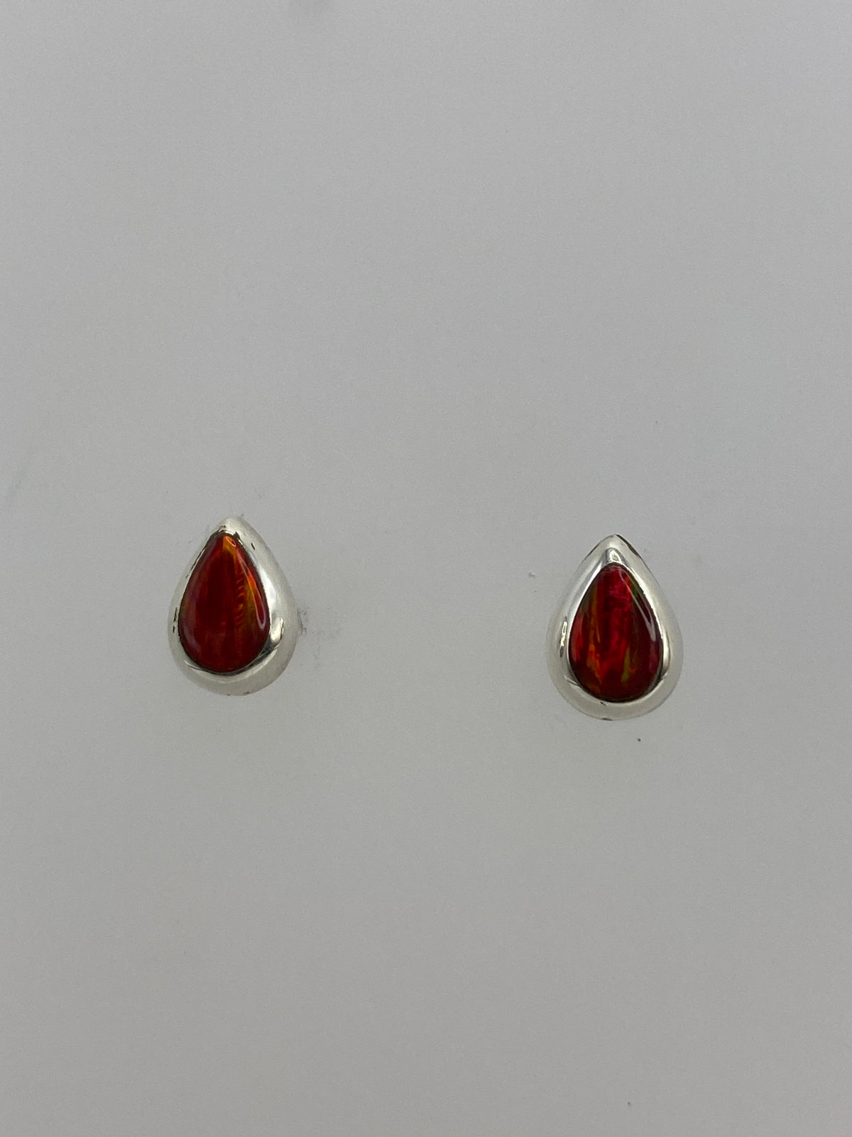 Par de aretes de plata con ópalo de fuego rojo engastado, vistos de frente sobre fondo blanco