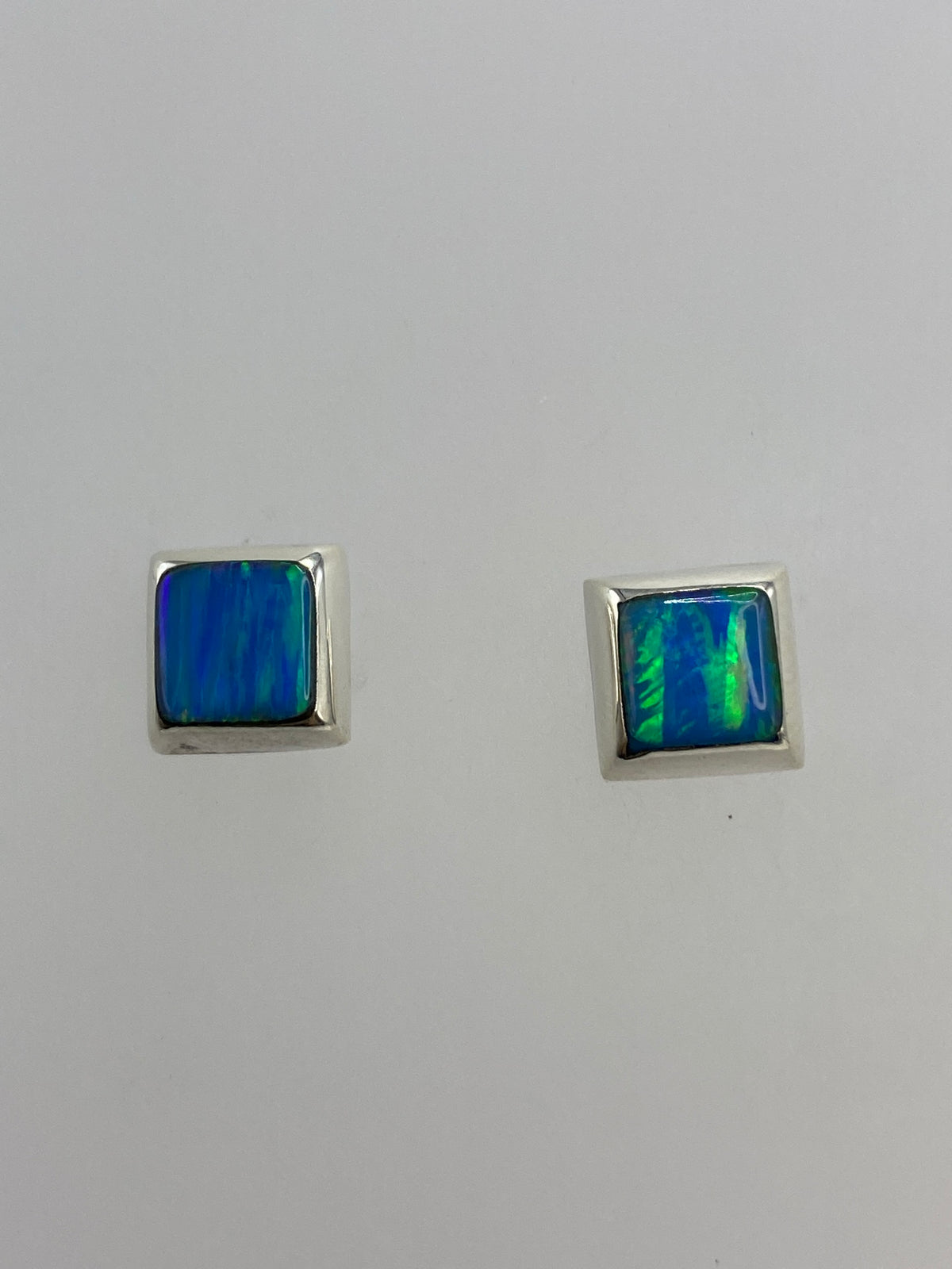 Par de aretes de plata con ópalo de fuego azul, reflejando luz en tonos azul y verde