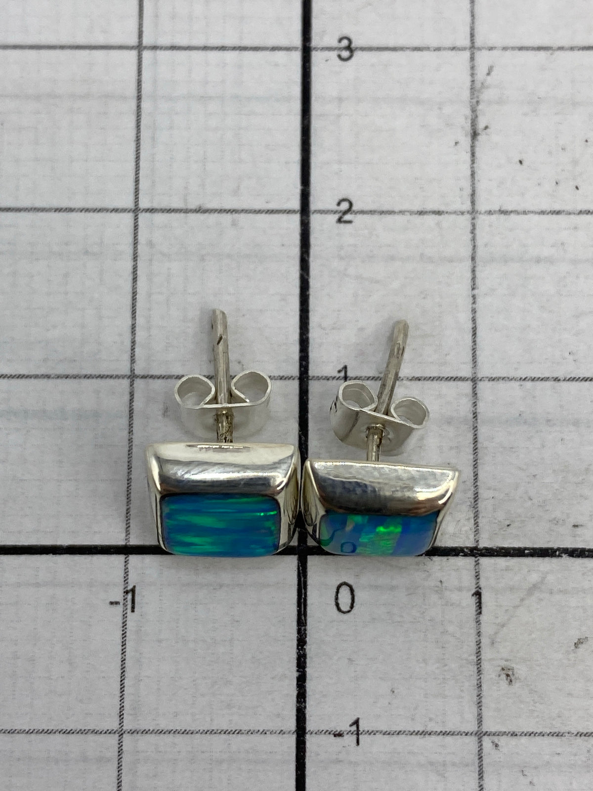 Aretes de plata con ópalo de fuego en la mano, demostrando el tamaño compacto de 1.3 cm