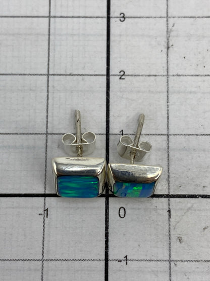 Aretes de plata con ópalo de fuego en la mano, demostrando el tamaño compacto de 1.3 cm