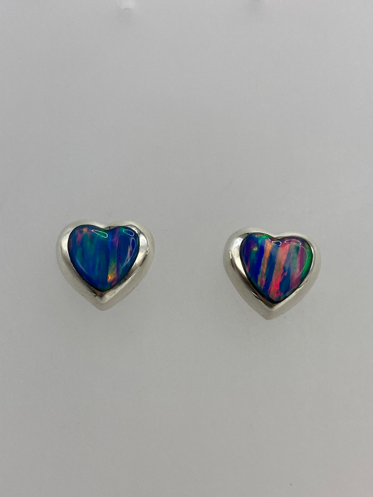 Detalle de los aretes mostrando los reflejos de fuego rojo, naranja y azul del ópalo engastado
