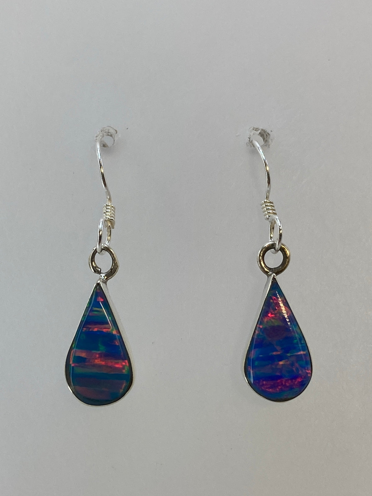 Par de aretes de plata con ópal de fuego multicolor mostrando reflejos azul, rojo y verde