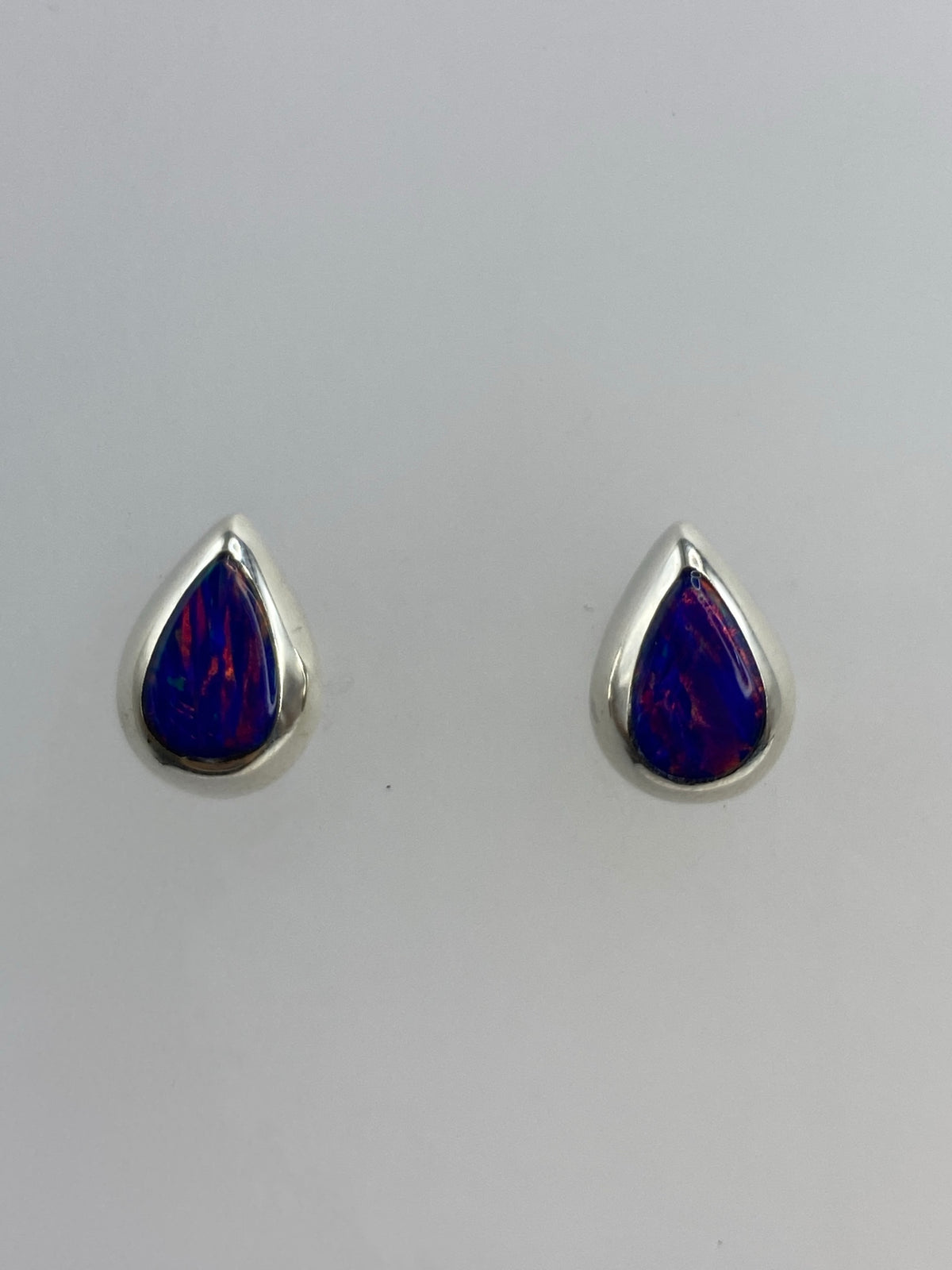 Par de aretes de plata 925 con ópalo de fuego morado, vistos de frente sobre fondo blanco