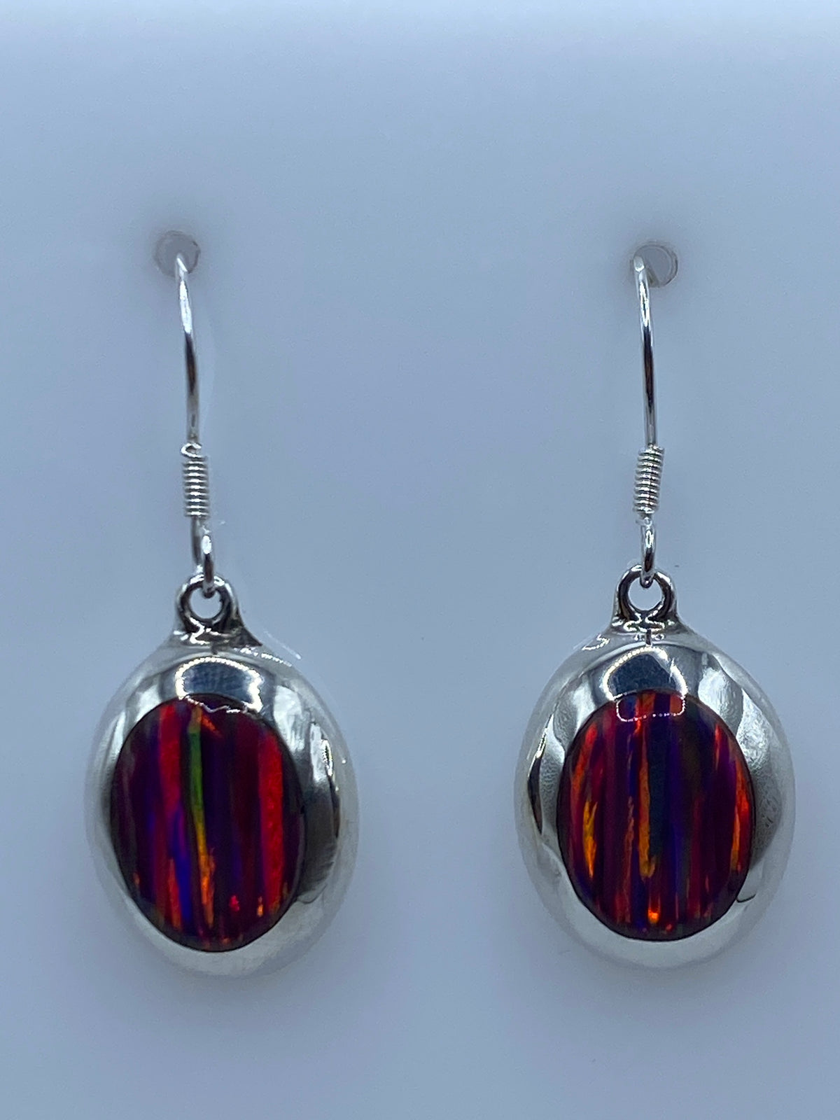 Par de aretes de plata con ópalo de fuego multicolor brillando en la luz