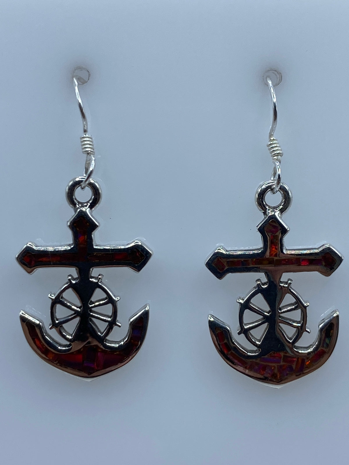 Aretes religiosos marineros mostrando la cruz y rueda náutica sobre el ópalo rojo