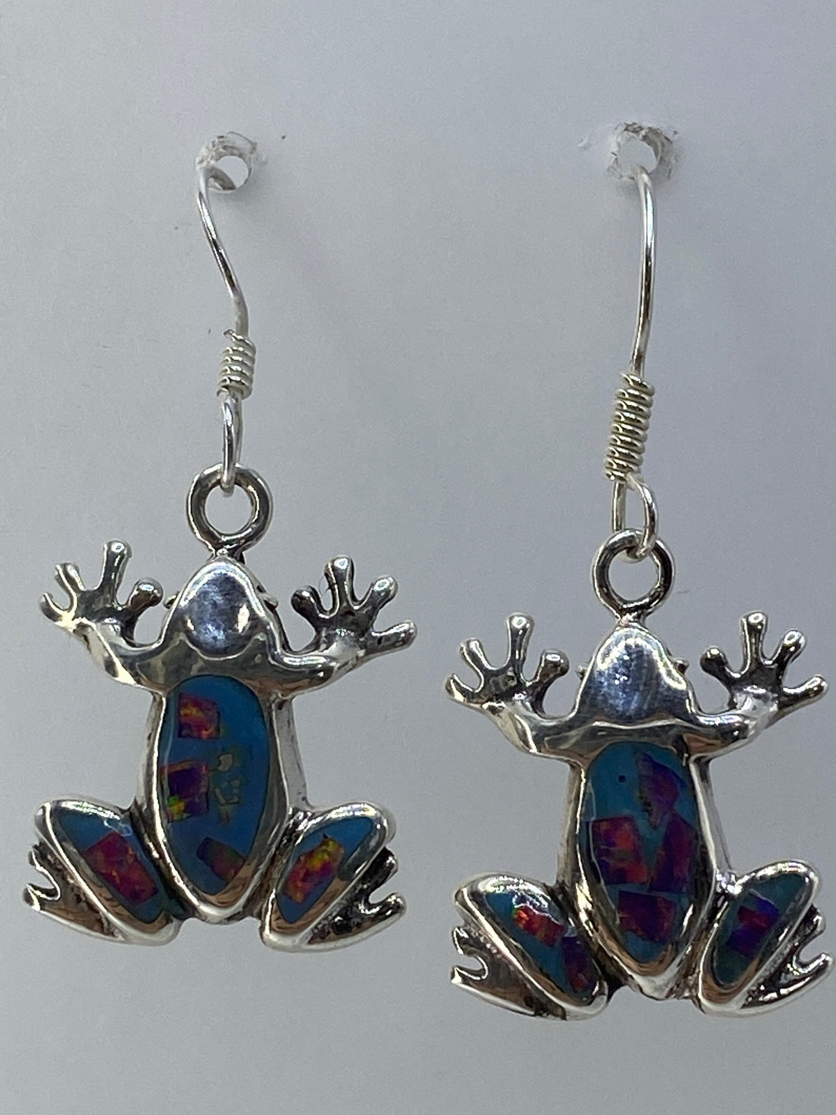 Aretes de rana colgando, mostrando los juegos de color rojo, verde y azul del ópalo