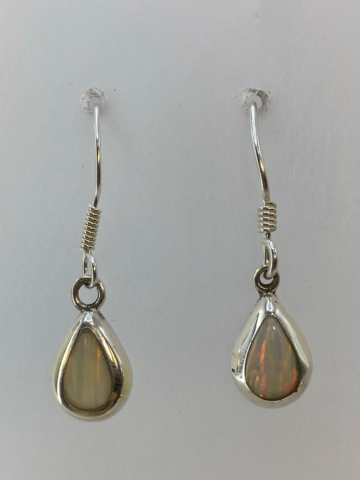 Par de aretes de plata 925 con ópalo de fuego multicolor, colgando sobre fondo blanco