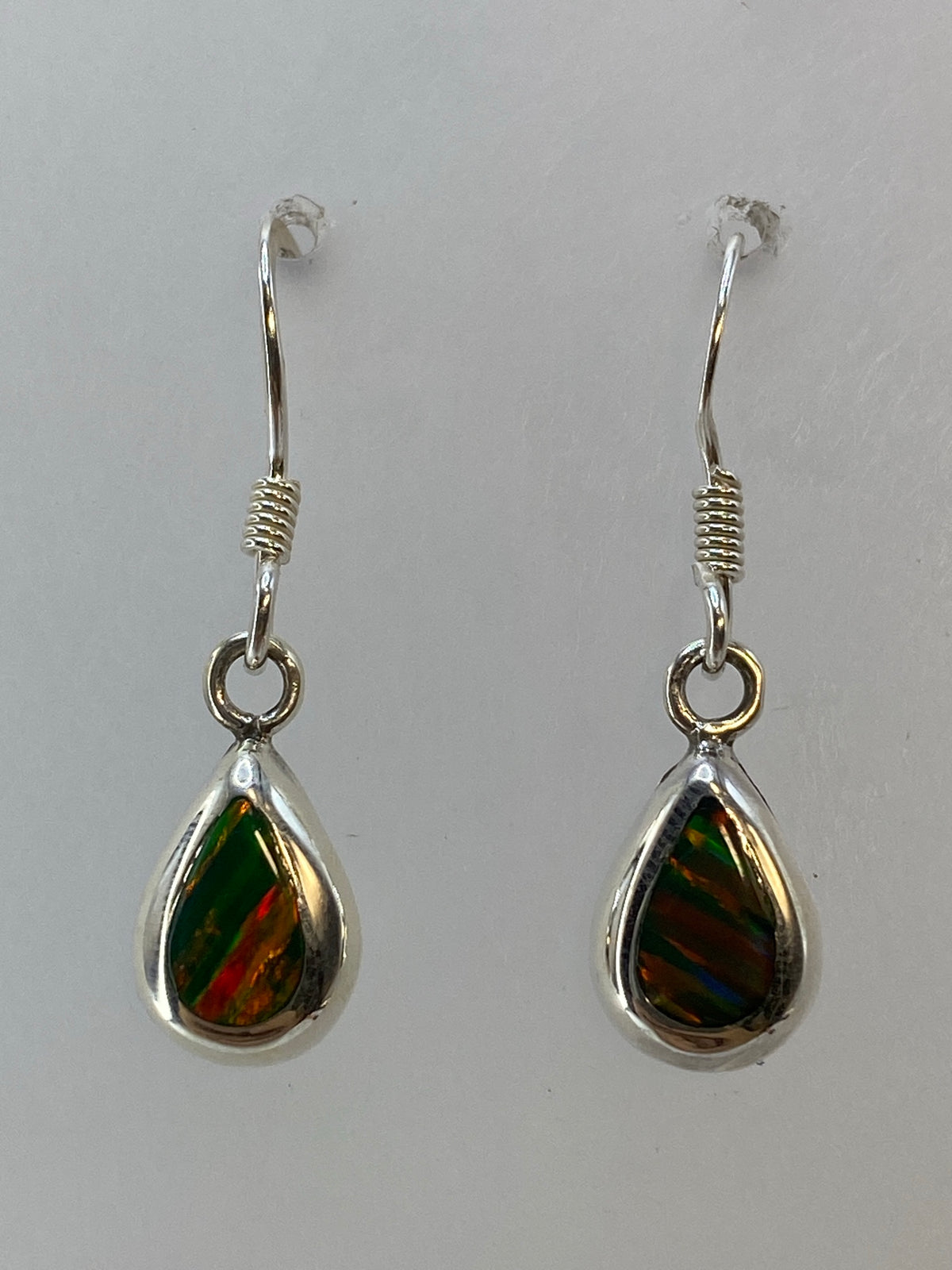 Aretes de plata con ópalo de fuego verde en forma de gota, colgando sobre fondo blanco