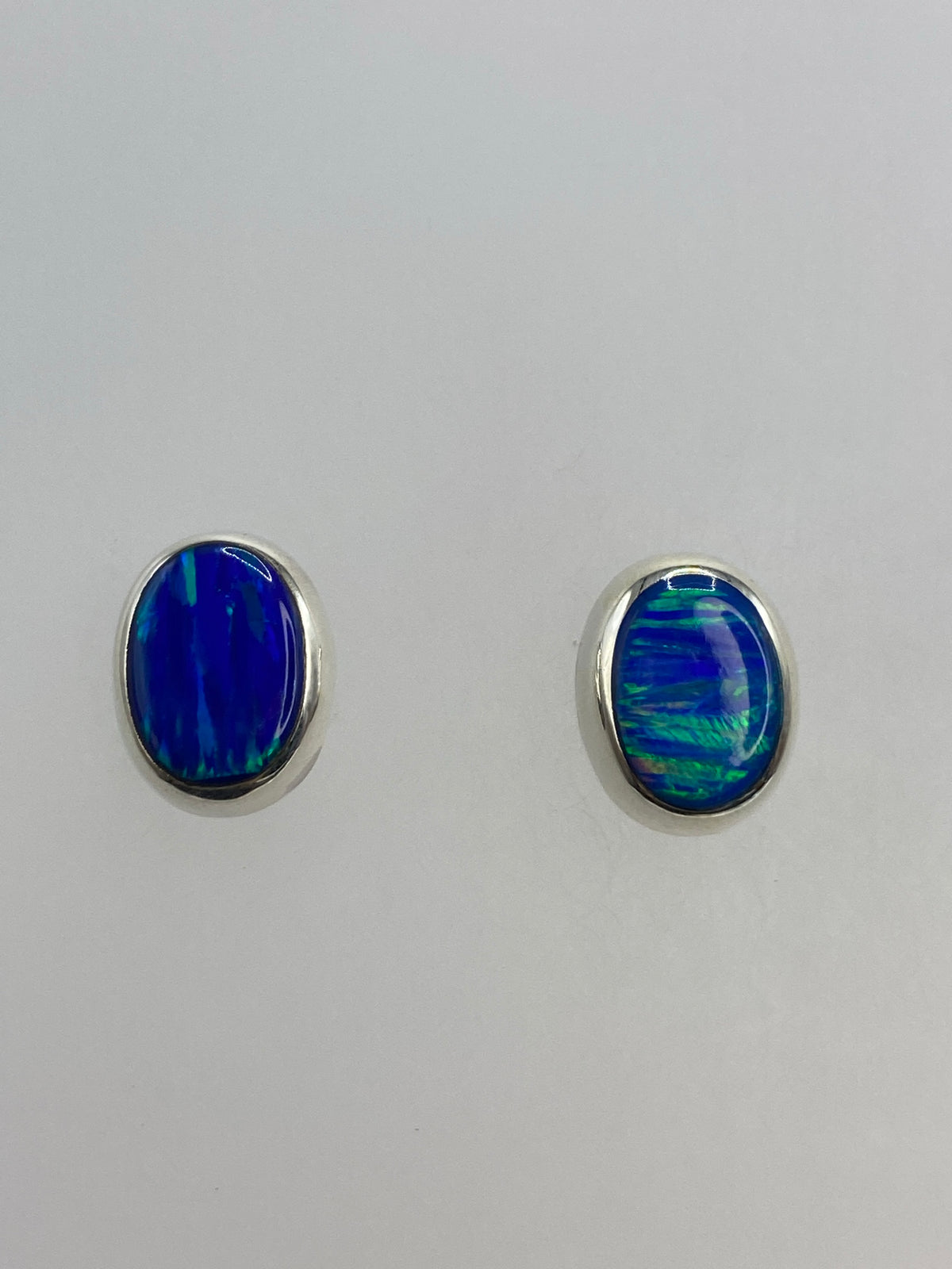 Par de aretes de plata con ópalo de fuego azul engastado, sobre fondo blanco