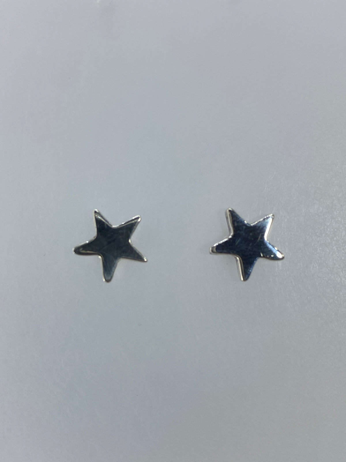 Aretes de plata minimalistas con estrella pulida sobre fondo blanco