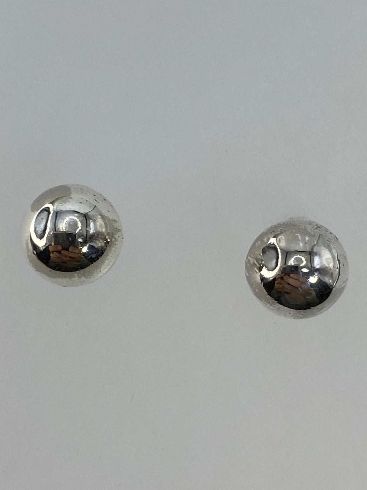 Aretes de bolita de plata sobre fondo blanco mostrando acabado pulido