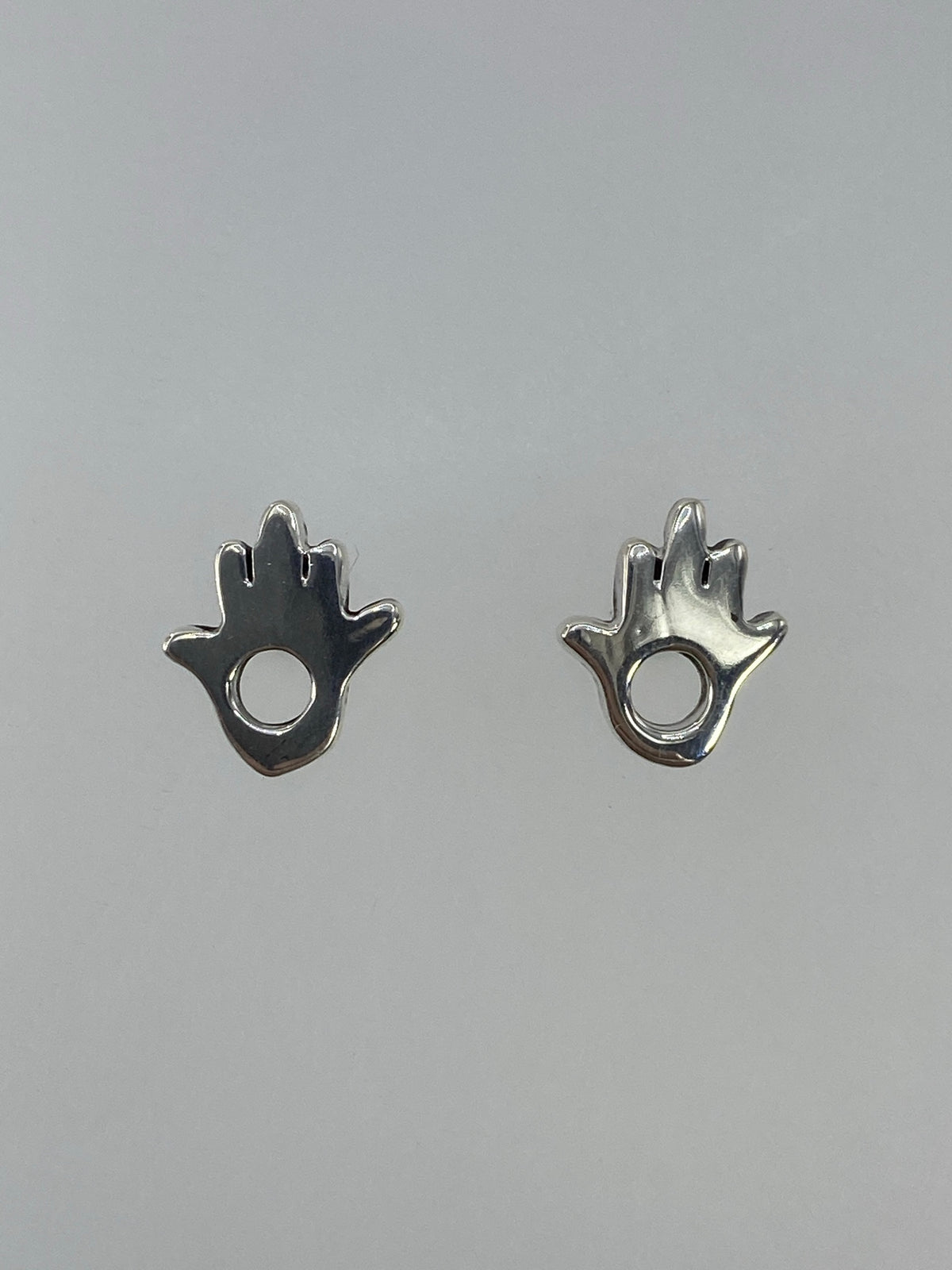 Detalle de los dos aretes de plata hamsa simétricos sobre fondo gris