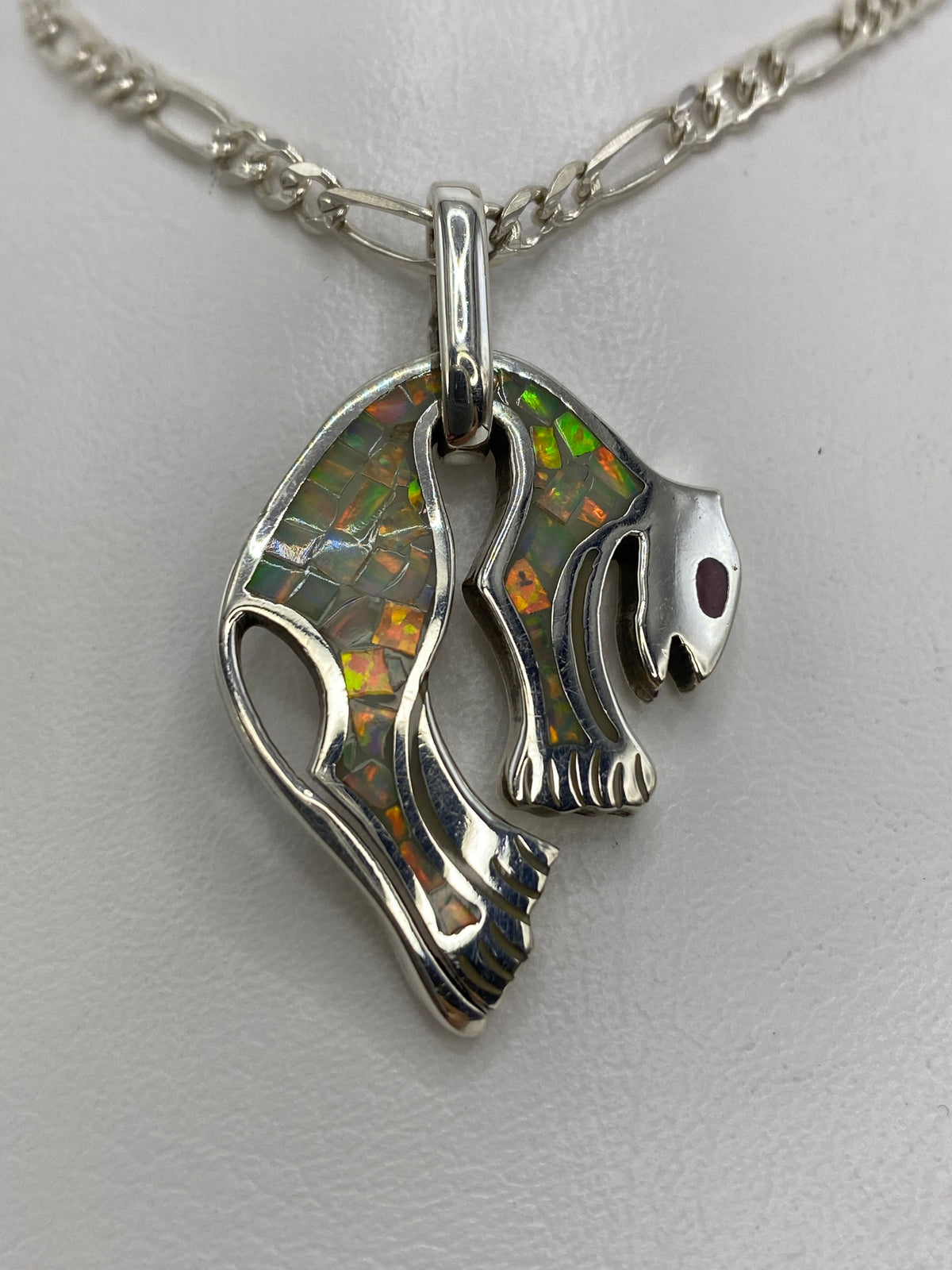 Dije de plata con diseño prehispánico (alas y calavera) engastado con ópalo de fuego blanco, colgado de cadena figaro en plata