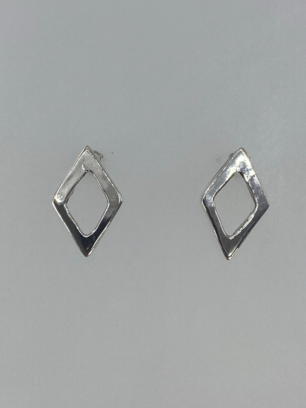 Aretes de plata cartoneado minimalista vistos de frente sobre fondo gris