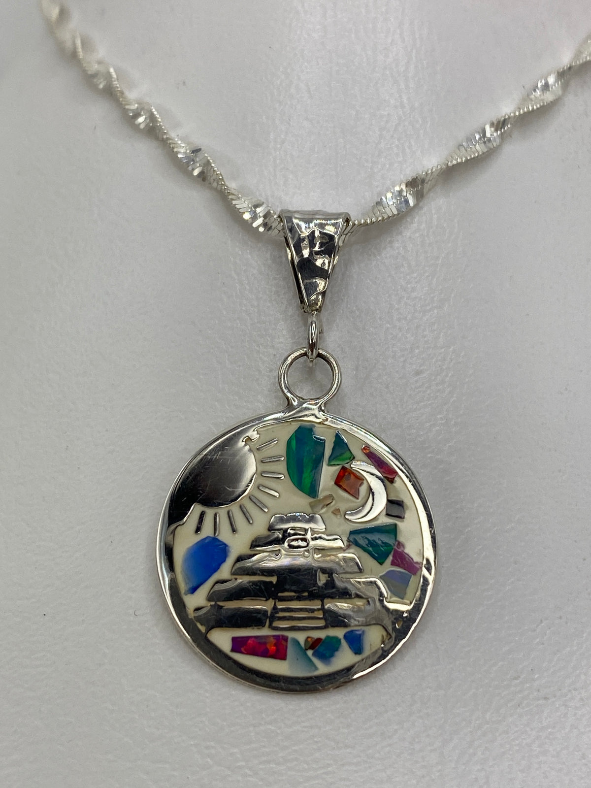 Dije de plata con ópalo de fuego multicolor y diseño prehispánico (sol, luna, pirámide) sobre fondo blanco