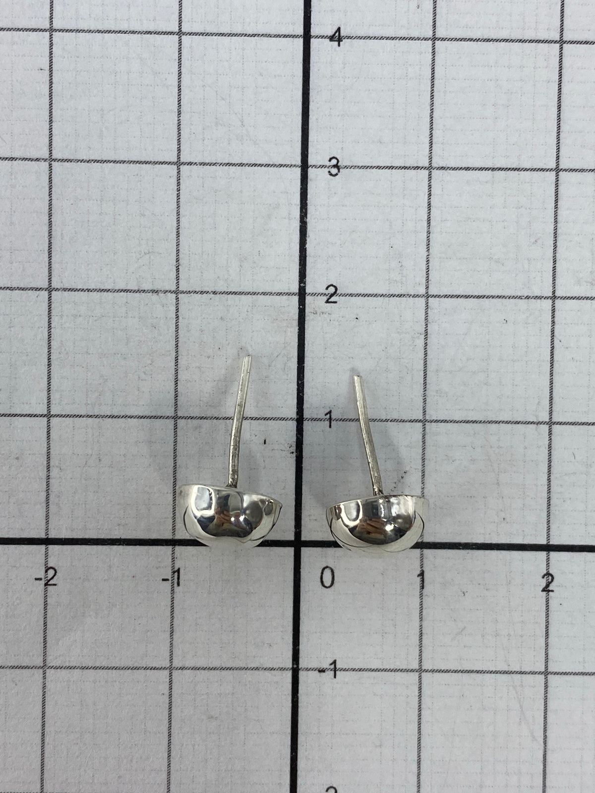 Aretes minimalistas en la mano, demostrando su tamaño compacto de 1.2 cm