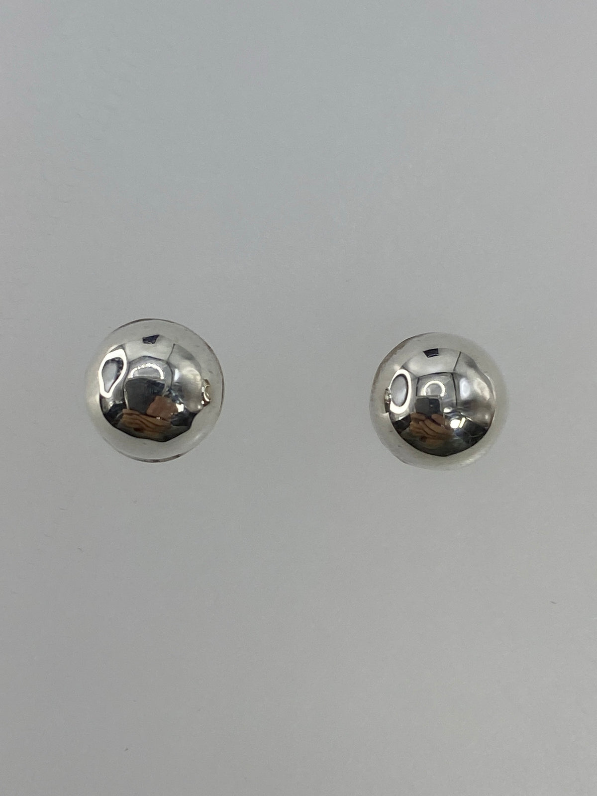 Par de aretes de plata cartoneado, diminutos y redondos, en fondo blanco
