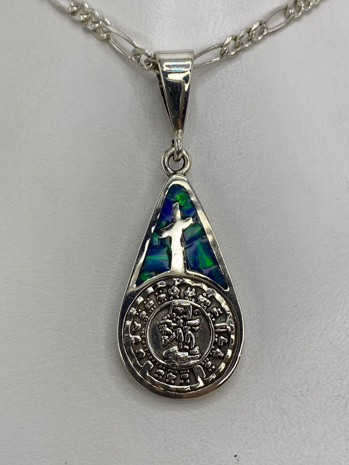 Dije de plata 950 con cruz y símbolo prehispánico, ópalo de fuego azul, sobre cadena figaro