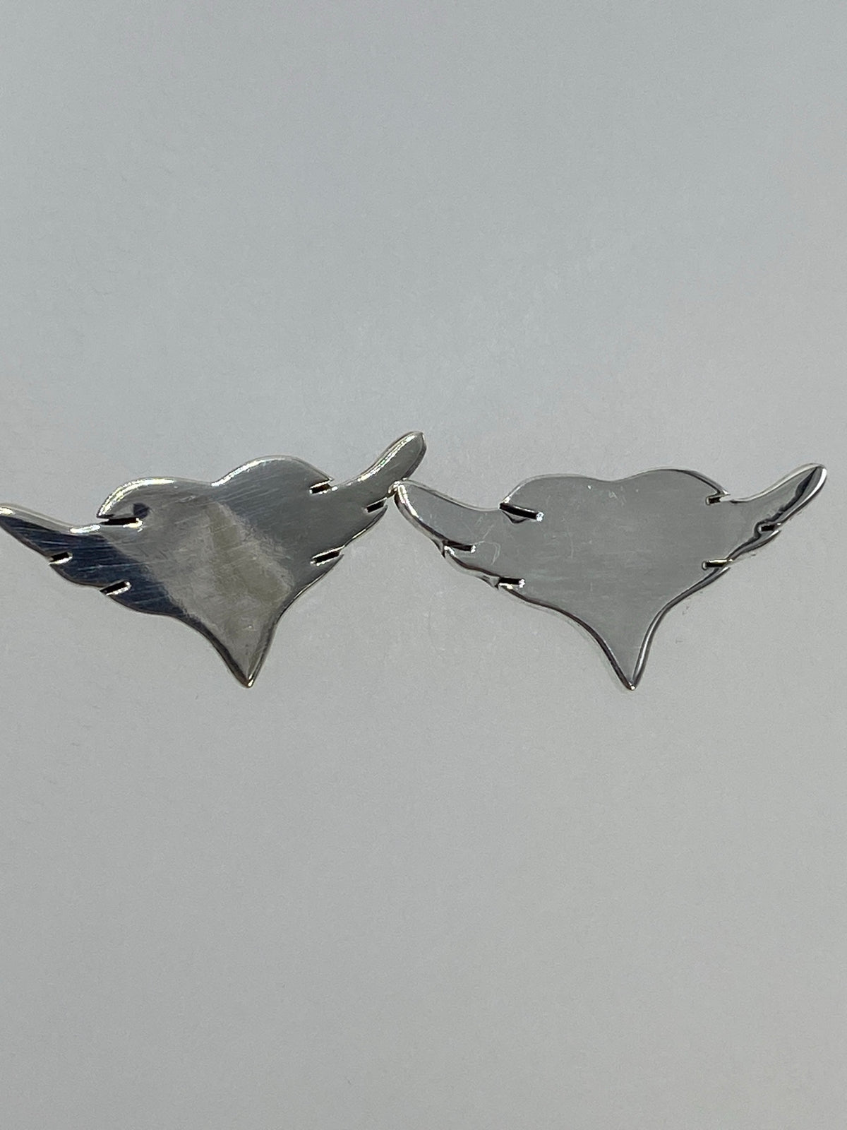 Aretes sobre fondo gris neutro mostrando el diseño simétrico de alas