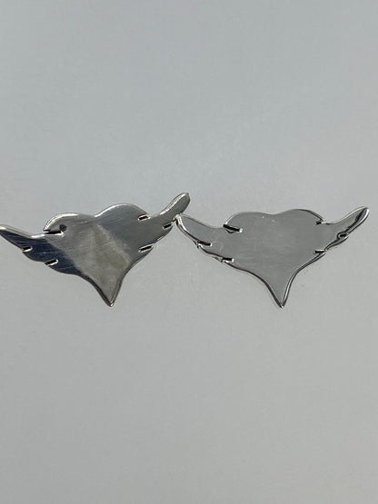 Aretes sobre fondo gris neutro mostrando el diseño simétrico de alas