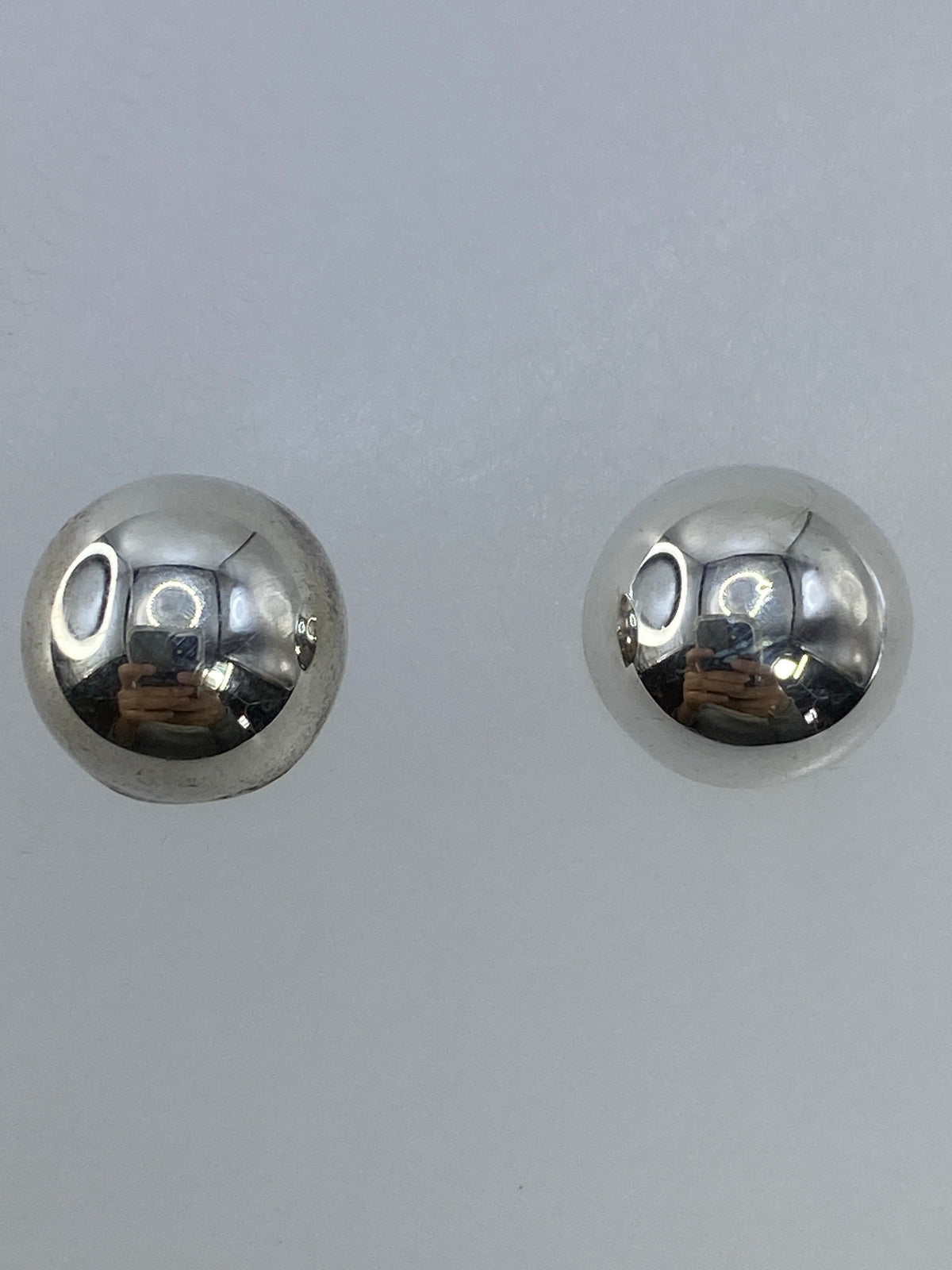 Aretes de plata minimalistas sobre fondo blanco, vistos de frente