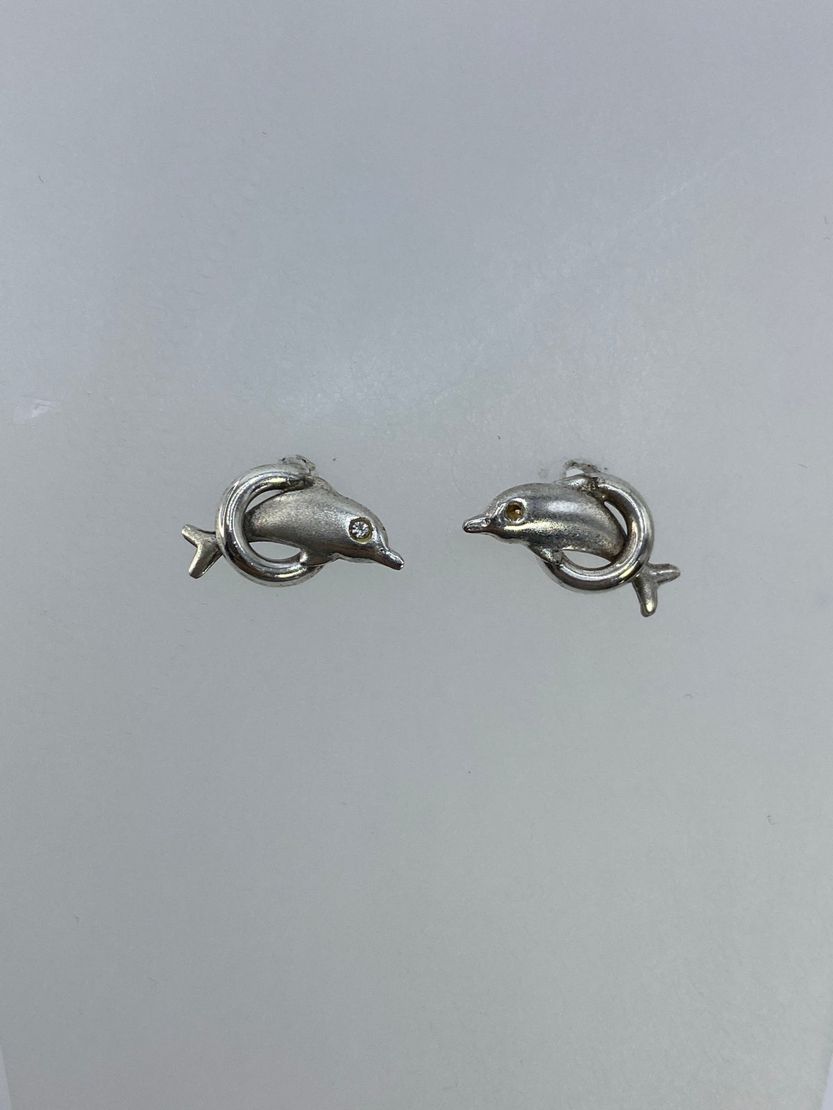 Detalle de los aretes delfín minimalistas en plata pulida