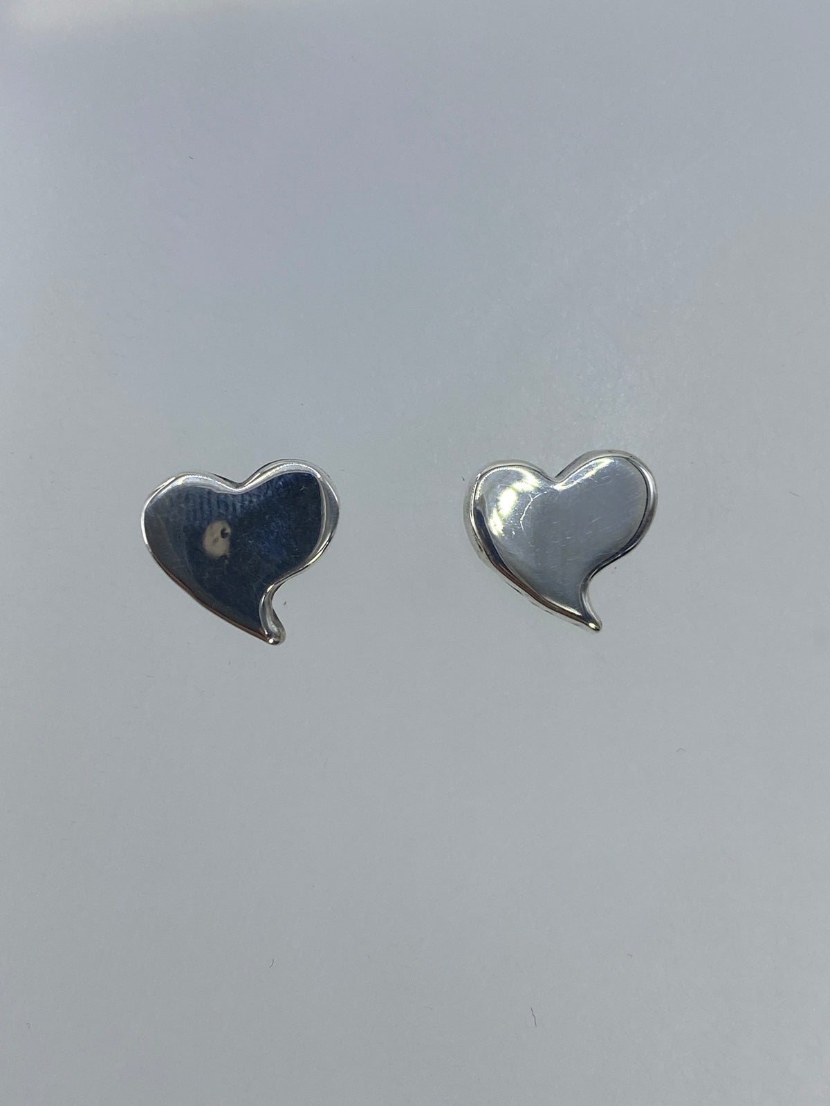 Vista frontal de los aretes corazón de plata pulida reflejando la luz