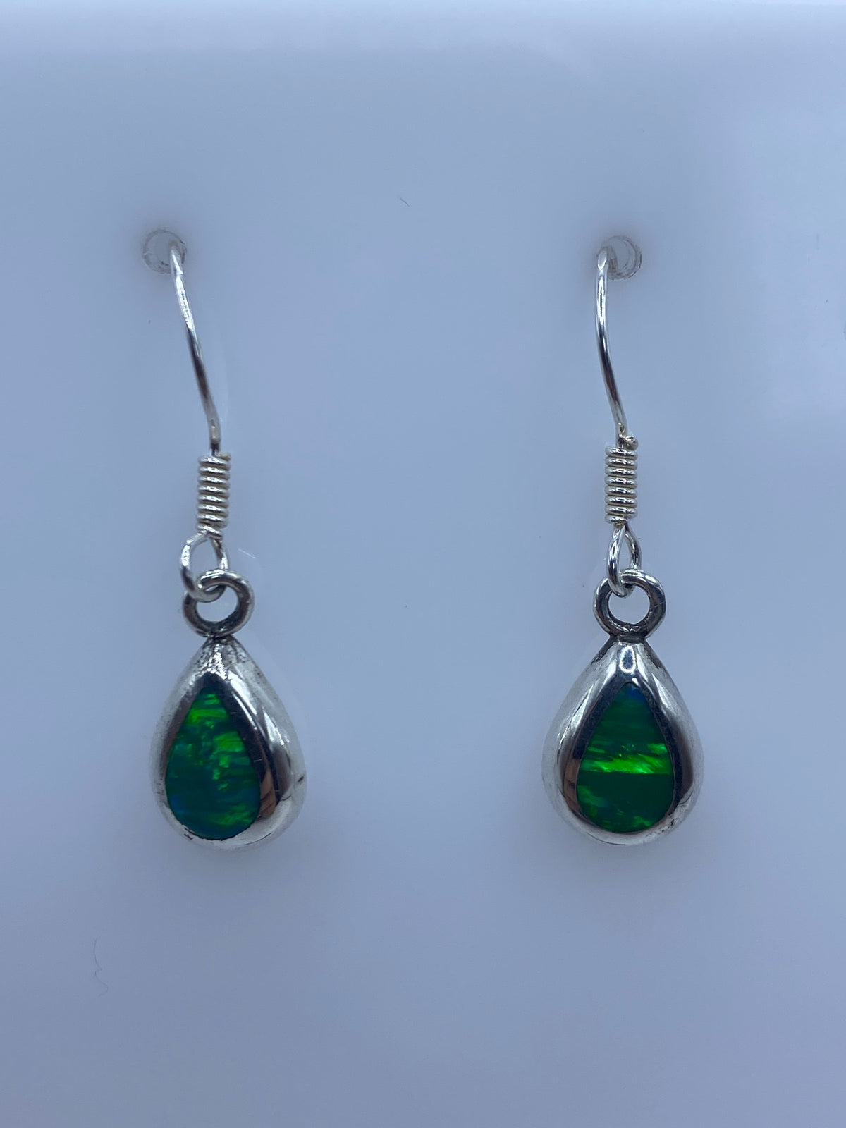 Detalle de un arete mostrando el engaste a mano y el brillo verde del ópalo