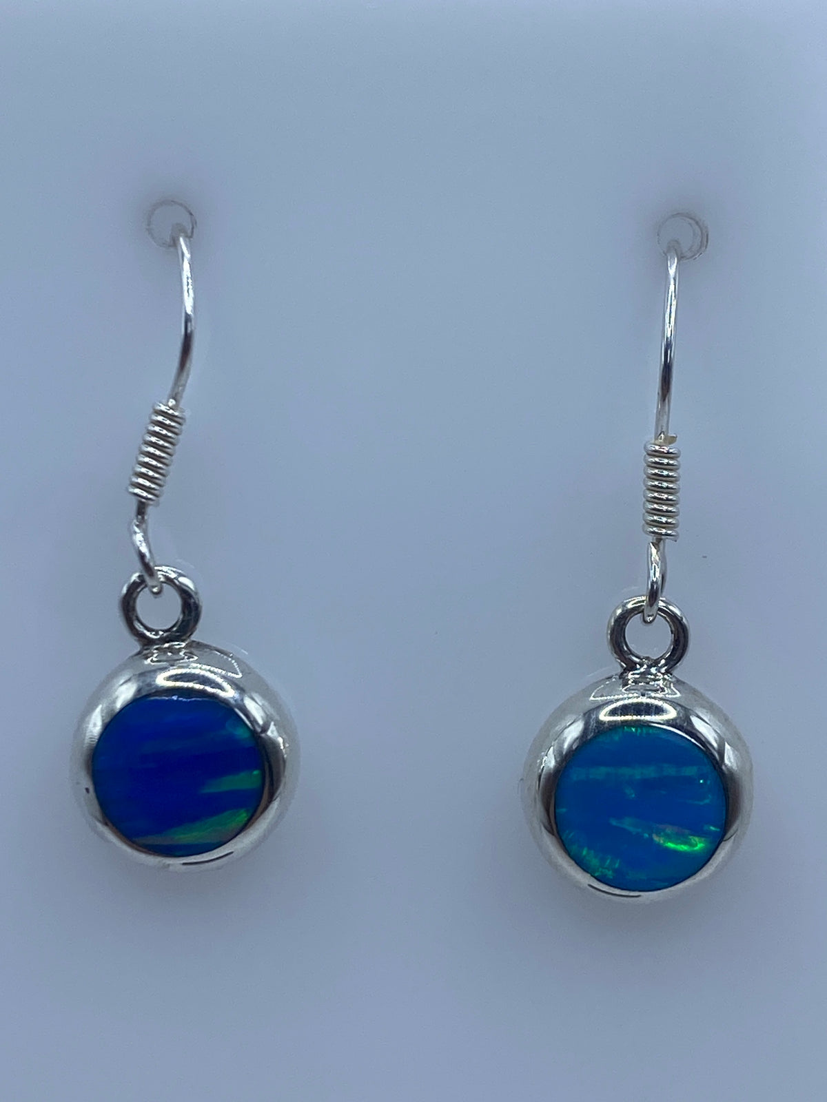 Detalle del engaste de Ópalo de Fuego azul en plata pura, vista frontal de los dos aretes