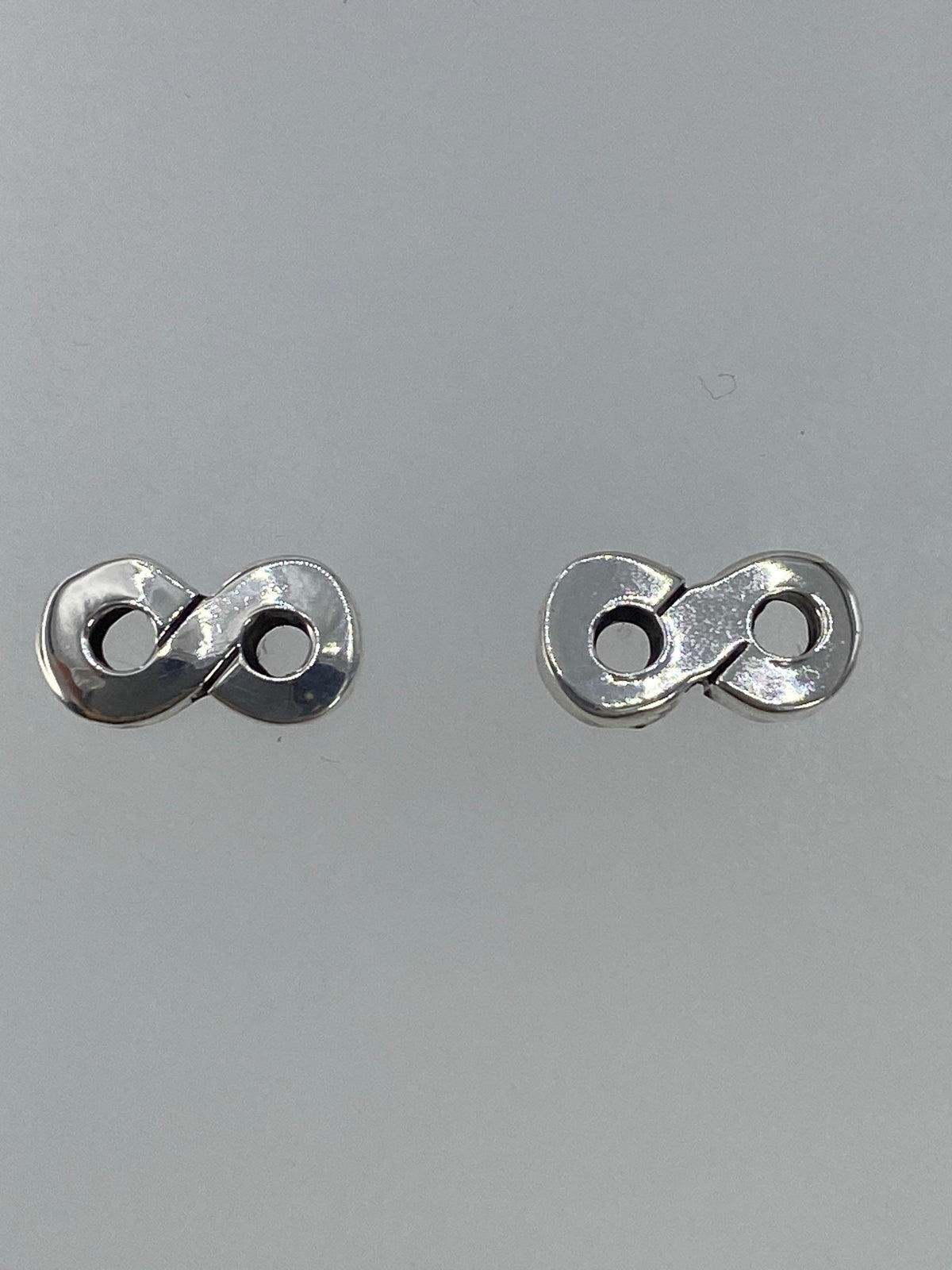 Par de aretes de plata cartoneado minimalista, vista frontal sobre fondo gris