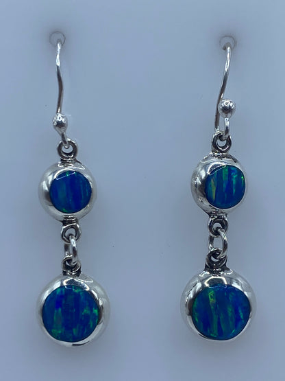 Par de aretes plata ópalo de fuego azul, incrustación a mano, colgando sobre superficie gris