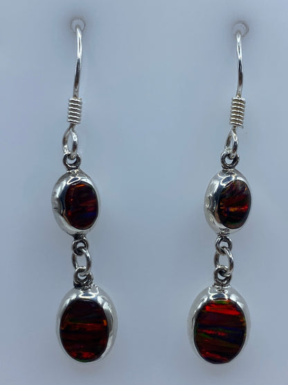 Par de aretes de plata con ópalo de fuego multicolor engastado, colgando sobre fondo gris