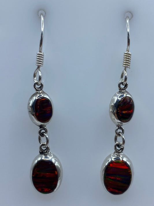 Par de aretes de plata con ópalo de fuego multicolor engastado, colgando sobre fondo gris