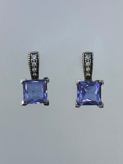 Par de aretes de plata con circonia azul engastada, vistos de frente sobre fondo gris