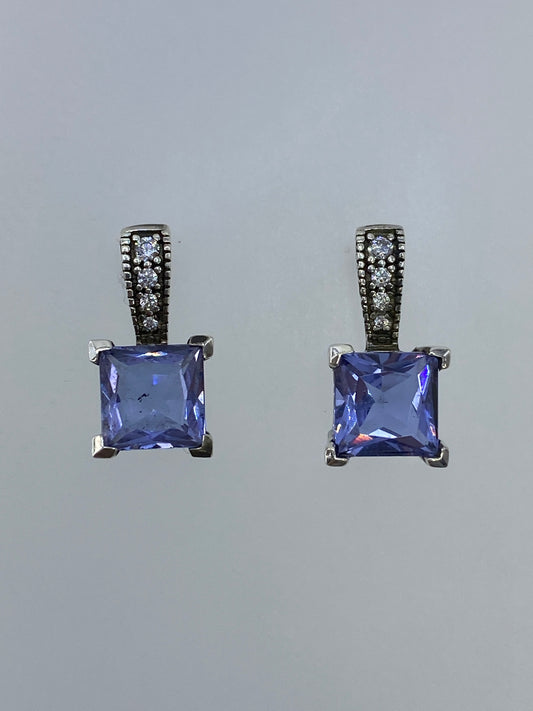 Par de aretes de plata con circonia azul engastada, vistos de frente sobre fondo gris